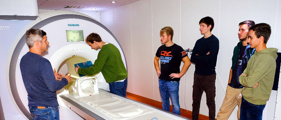Teaser: Schüler stehen mit einem Wissenschaftler vor einem Kernspintomographen.