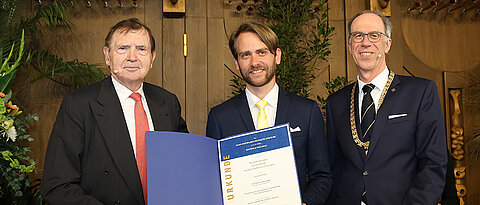 Baldwin Knauf (l.) überreicht den Baldwin und Inge Knauf-Förderpreis mit JMU-Präsident Paul Pauli an Dr. Tobias Huber-Loyola.