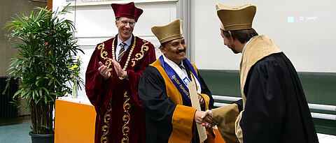 Dekan Holger Helten (re.) und Präsident Paul Pauli (li.) gratulieren Professor Jarugu Narasimha Moorthy zum Erhalt der Ehrendoktorwürde.